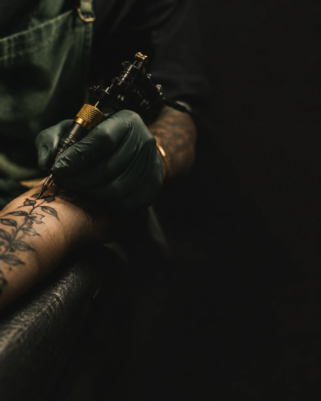 Tattoo artist's hands tattooing fine-line floral linework on a client's forearm